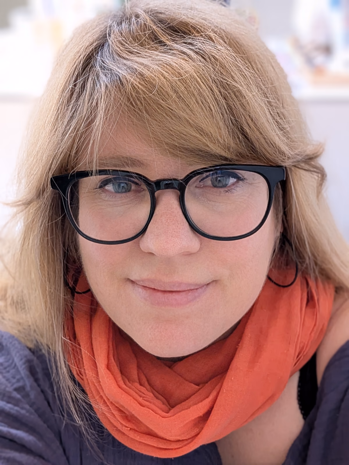 Portrait of Silke Voigts wearing glasses and an orange scarf.